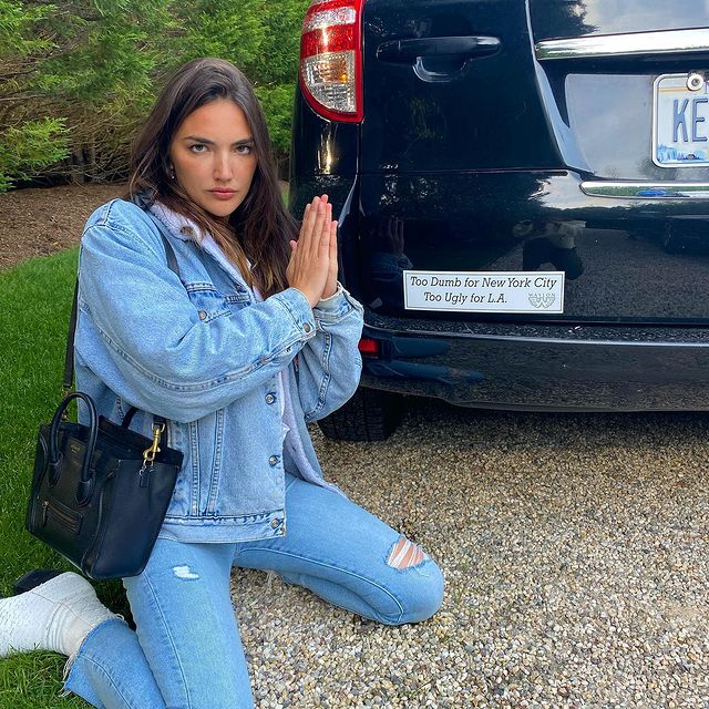 Hailee Keanna Lautenbach in a blue denim jacket and jeans joining her hands behind her black car.